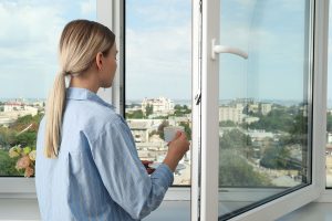 Mujer tomando cafe mientras abre sus ventanas batientes de pvc en Madrid